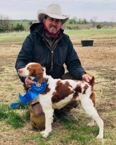 Professional Bird Dog Trainer & Handler, Scott Johnson, kneeling on the ground with one of his dogs and a blue ribbon